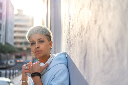 Portrait of fashionable young woman wearing blue hoodie posing on the city wall. Blonde girl in...