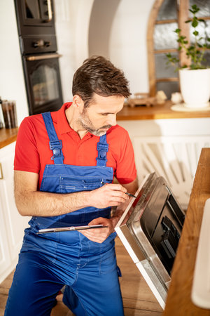 Plumber repairing a dishwasher in a kitchen. Worker during his work.の写真素材