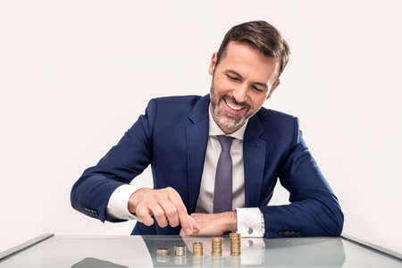 Smiling handsome businessman Put Coin To Stack Of Coins. Conceptual photo. Studio shot.