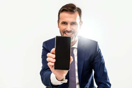 Handsome smiling businessman showing phone with blank black screen to the camera. Man holding smart mobile cell phone in hand. A lot of copy space.の写真素材
