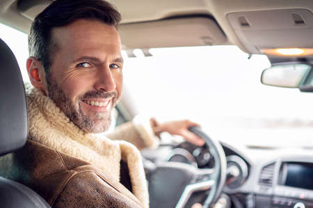 Handsome smiling man driving new car, enjoying a road trip, looking at the camera. A lot of copy space.の写真素材