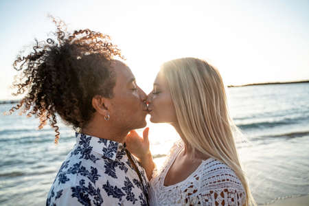 Multiethnic couple kissing, having fun together, dating on the beach during sunset. People in love. Honeymoon. Real emotions. Happiness.の写真素材