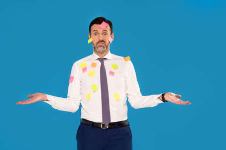 Tired male businessman in formal clothes posing over blue studio background, a lot of stickers on his body. Worker. Real people.の写真素材