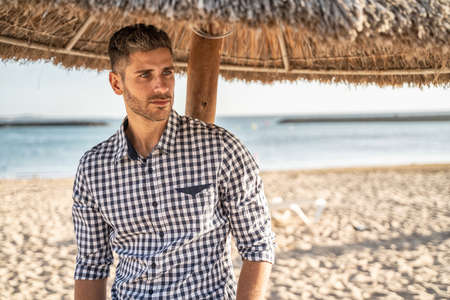 Handsome young italian man posing on the beach ,, wearing fashionable shirt, summer time. A lot of copy space.の写真素材