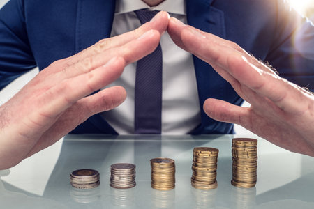 Close-up photo Of Businessperson Protecting Stack Of Coins With Hands At Desk.の写真素材