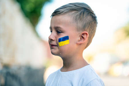 Child against war. Upset Ukrainian boy with bue yellow flag on his face, crying, protesting war conflict. Evacuation of civilians. Freedom to Ukraine. Stop Russian aggression. Stop war Ukraine Russia. Support Ukraine.の写真素材