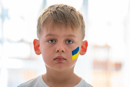Child against war. Upset Ukrainian boy with bue yellow flag on his face protesting war conflict. Evacuation of civilians. Freedom to Ukraine. Stop Russian aggression. Stop war Ukraine Russia. Support Ukraine.の写真素材