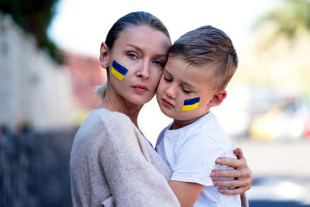 Families against war. Upset Ukrainian boy with his mother, with bue yellow flag on his face,  protesting war conflict. Evacuation of civilians. Freedom to Ukraine. Stop Russian aggression. Stop war Ukraine Russia.の写真素材