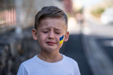 Child against war. Upset Ukrainian boy with bue yellow flag on his face, crying, protesting war conflict. Evacuation of civilians. Freedom to Ukraine. Stop Russian aggression. Stop war Ukraine Russia. Support Ukraine.の写真素材