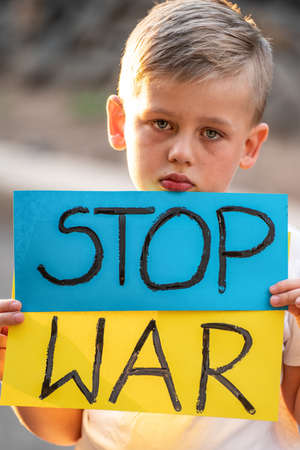 Child against war. Upset Ukrainian boy with blue yellow flag with stop war sign , protesting war conflict on the blue wall. Evacuation of civilians. Freedom to Ukraine. Stop Russian aggression. Support.の写真素材