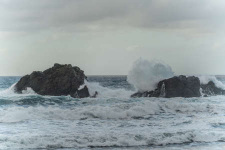 Beautiful ocean view with large powerful waves splashing on the rocks. Cloudy sky. Landscape.の写真素材