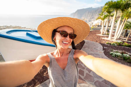 Happy woman in summer hat smiling to the camera, taking selfie on Tenerife, Los Gigantes. Canary islands. View point. Tourism. Tourist. Travel.の写真素材