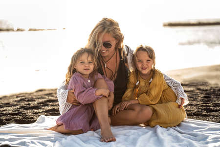 Cute happy little sisters playing with her mother outside. Woman and her daughters relaxing on the sunny beach. Happy family. Happy Mother's Day. Motherhood, childhood. Summer vibes.の写真素材