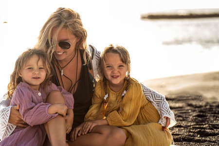 Cute happy little sisters playing with her mother outside. Woman and her daughters relaxing on the sunny beach. Happy family. Happy Mother's Day. Motherhood, childhood. Summer vibes.の写真素材