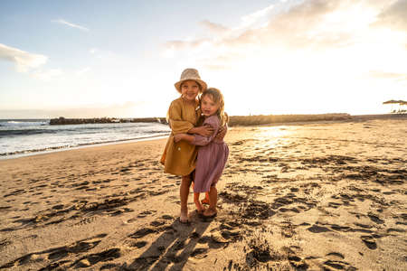 Kids playing on the beach. Little sisters having fun at sea shore at sunset. Family summer vacation vibes. A lot of copy space.の写真素材