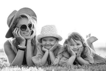 Beautiful photo of cute happy little sisters playing with her mother outside. Woman and her smiling daughters lying on the green grass in the park. Happy family. Happy Mother's Day. Motherhood, childhood. Summer vibes.の写真素材