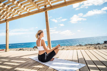 Yoga and meditation concept. Woman meditating on the ocean coast. Girl practicing mindfulness to clear her mind.の写真素材