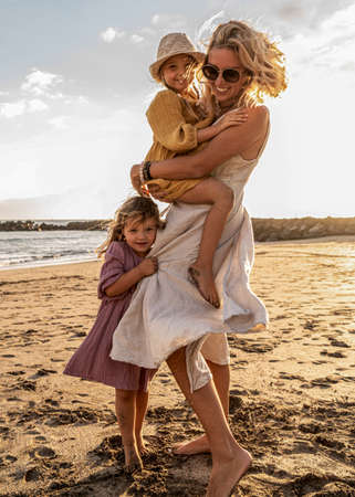 Happy beautiful family relaxing and walking at the sunset beach in summer. Smiling mother with her two little daughters having fun on vacations. Real people lifestyle.の写真素材