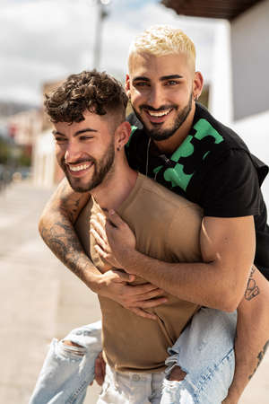 Portrait of a happy gay couple having fun on an outdoor date, playing together, smiling. Real people emotions. Handsome guys.の写真素材