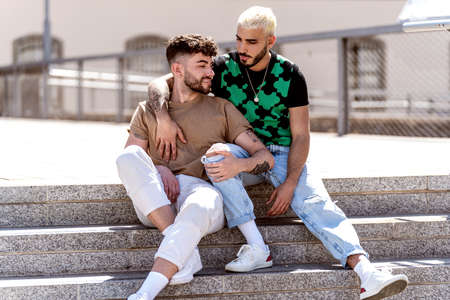 Fashionable gay couple on an outdoor date, spending time together, talking and smiling. Real people lifestyle. Handsome guys.の写真素材