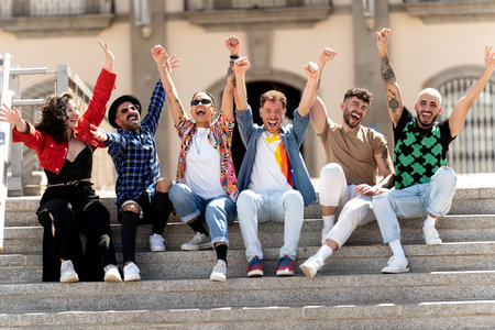 Multiracial group of happy young friends laughing together and having fun sitting near the university. Students celebrating success. Unity and community concept. Real people emotions and lifestyle.の写真素材