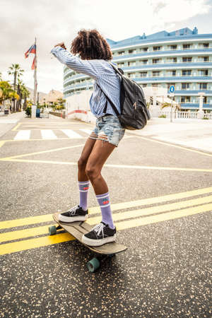 Crazy woman with afro hairstyle riding on a skateboard. Skateboarding on the city street. Hipster. Lifestyle. Hobby.の写真素材