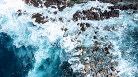Top view of the huge ocean waves crashing on the rocky shore. Power of the ocean. Aerial view of the...