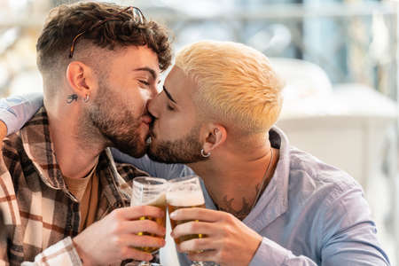 Fashionable gay couple on a date, spending time together, kissing, drinking beer. Real people lifestyle. Love. Handsome guys.の写真素材