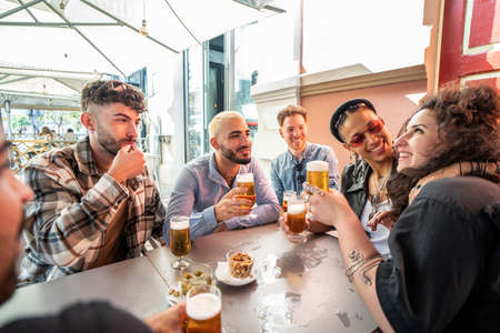 Group of friends drinking beer at brewery bar and talking, smiling. Young millenial students having fun together. Friendship concept.の写真素材