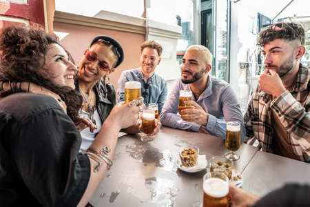 Group of friends drinking beer at brewery bar and talking, smiling. Young millenial students having fun together. Friendship concept.の写真素材