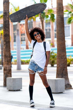 Happy girl with beautiful smile in trendy street style clothes enjoying riding skateboard at sunny day. Real people lifestyle. Hobby. Happiness.の写真素材