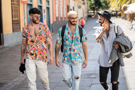 Three happy young men walking in the city, talking to each other, having fun. Multiethnic group of friends. Real people lifestyle.の写真素材