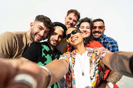 Group of happy young friends having fun and laughing while taking a selfie with mobile phone. Diverse millennial people spending time together. Friendship concept. Real people lifestyle.の写真素材