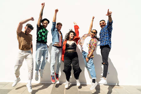 Group of happy young friends having fun and laughing, jumping over white wall. Diverse millennial people spending time together. Friendship concept. Real people lifestyle.の写真素材