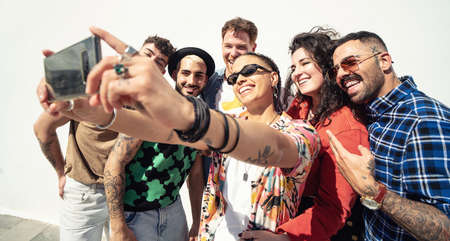 Group of happy young friends having fun and laughing while taking a selfie with mobile phone. Diverse millennial people spending time together. Friendship concept. Real people lifestyle.の写真素材