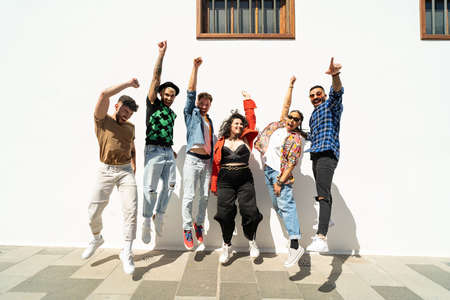 Group of happy young friends having fun and laughing, jumping over white wall. Diverse millennial people spending time together. Friendship concept. Real people lifestyle.の写真素材