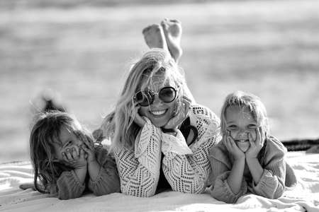 Happy woman relaxing with her two daughters outdoor on the beach, lying, talking and smiling. Mother's day. Children's day. Real people emotions.の写真素材