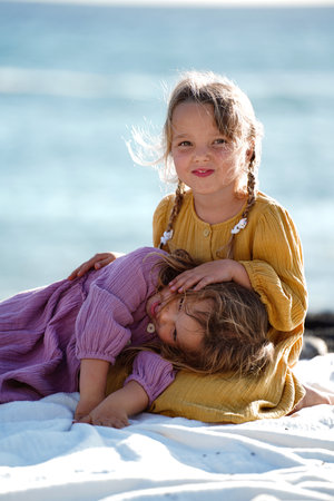 Happy little cute girls enjoying sunny day at the beach, hugging and smiling to the camera. Family summer vacation. Sister's love. A lot of copy space.の写真素材