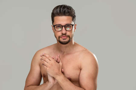Beauty portrait of handsome shirtless muscular young man wearing fashionable eyeglasses, looking at the camera, isolated over studio background. Healthy eyesight. A lot of copy space.の写真素材