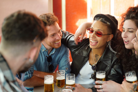 Friends talking and having fun together in the bar, drinking beers. Multicultural group of students. Real people emotions. Lifestyle.の写真素材
