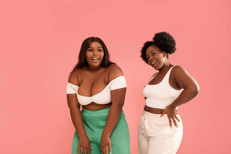 Studio shot of happy dark skinned, young sisters enjoying good moment, dancing and having fun together, posing over pink pastel studio background. Friendship and real people emotions concept. Body positive. Copy space.の写真素材