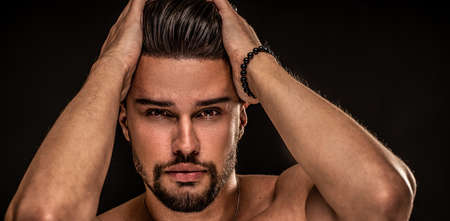Beauty portrait of sexy handsome bearded man with brown eyes looking at the camera. Black studio background. A small model.の写真素材