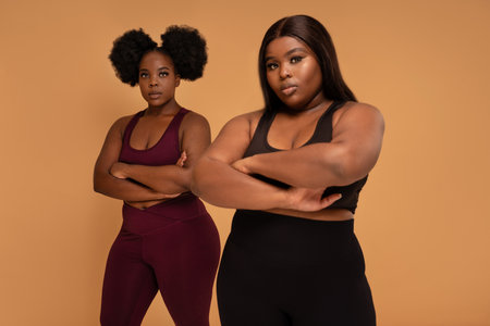 Active two plus size femal fitness trainers posing in fashionable sporty clothes together, looking at the camera. Real people lifestyle. Gym, healthy lifestyle concept. Body acceptance.の写真素材