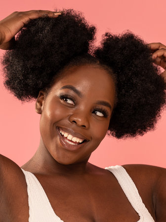African Woman with natural makeup and fashionable hairstyle posing on a pastel pink Studio Background. Real people emotions, toothy smile. Beauty closeup portrait.の写真素材