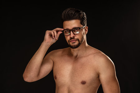 Handsome sensual man with brown eyes wearing eyeglasses, posing shirtless on black studio background. Copy space. Muscular body.の写真素材