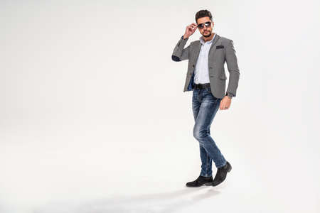 Full length photo of handsome man wearing jeans, shirt, elegant jacket and sunglasses. Men's beauty, fashion. Studio shot. Copy space.の写真素材