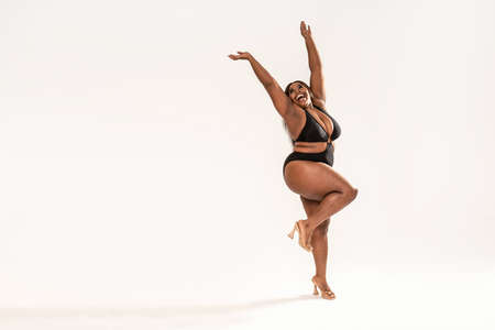 Full photo of happy, wonderful plus size African girl wearing black fashionable swimsuit, laughing and dancing.Concept of body acceptance, body positivity and diversity. Love your real body. Girl power.の写真素材