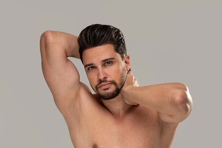 Studio beauty portrait of a handsome, sexy man with beard looking at the camera. Gray background. Copy space.の写真素材