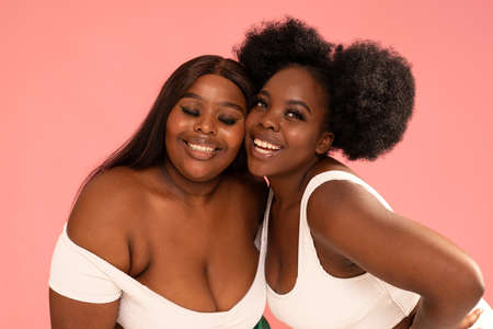Two beautiful happy women with amazing toothy smiles posing together on pink pastel studio background. Real people emotions. Friendship and happiness.の写真素材