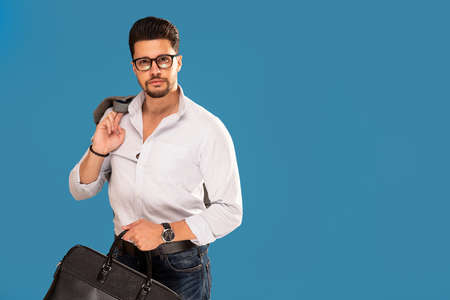 Handsome fashionable young businessman posing on blue studio background. A lot of copy space for...